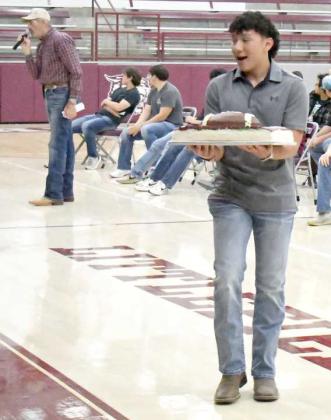 Littlefield sophomore, Ian Mendez, shows off his cake, while Auctioneer Guyle Roberson auctions it off during the 2023 LHS Cake Auction that took place Friday morning at Wildcat Gymnasium. (Staff Photo by Derek Lopez)
