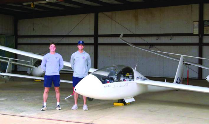 Instructors Matt Withers (left) and Creed Thompson (right), part of the USAF Academy’s 94th line training squadron, are standing beside a TG15A training glider inside a hangar, where aircraft are stored and maintained between flights. (Photo by Leon Szaniszlo)