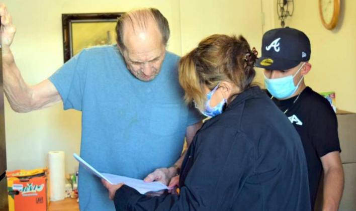 GOING OVER PAPERWORK – Mr. Edwards goes over the paperwork with Patricia Gonsalez, during the delivery of his food at the XIT Apartment. Adrian Reyes looks on. (Photo by Ann Reagan)