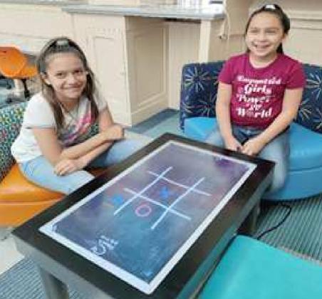 TIC TAC TOE GAME – These two girls were enjoying playing games on the new Interactive Touch Table at Lamb County Library in Littlefield. This new gaming table has 14 built-in games, including Tic Tac Toe, Pong, Air Hockey, Match, Paint, and Quizzes, and more. (Lamb County Library Photo)