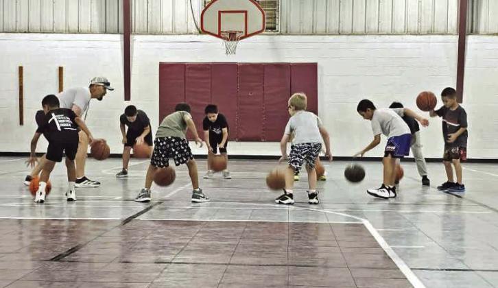Littelfield varsity basketball coach, Nathan McKinnon, goes over different types of dribbles with an older group of campers, during the first day of basketball camp on Monday, June 8th. (Staff Photo by Derek Lopez)