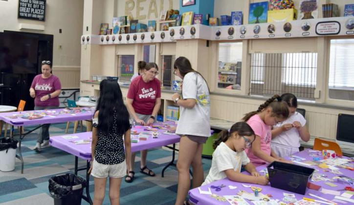 Volunteers help set up tables as attending kids work on making their own custom bookmarks at the Lamb County Library’s craft night on July 9.