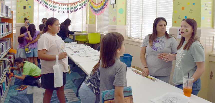 Summer Reading program attendees are assisted by volunteers Rebecca and Analeeze De La Rosa at the Puzzle Necklace craft station on Wednesday, June 7, 2023. (Photo by Ann Reagan)