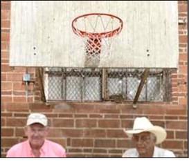 Two remaining members of late Coach Walter Chambers’ Burkett High School basketball team stand in front of the backboard, still attached to the wall of gymnasium constructed in 1937. Shown are Pat DeBusk, left, and Dick Koenig.