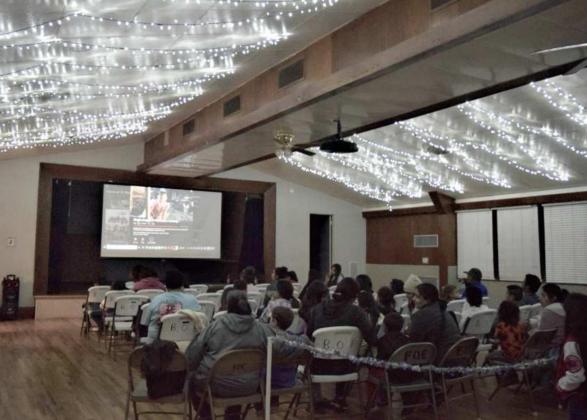 Beneath twinkling lights, families settle in to enjoy the movie”Jingle Jangle” at Our Place Friday night. December 10, 2021. (Photo by Ann Reagan)